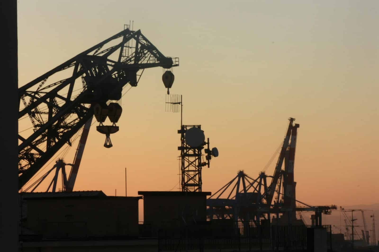 silhouette of metal cranes at worksite during golden hour